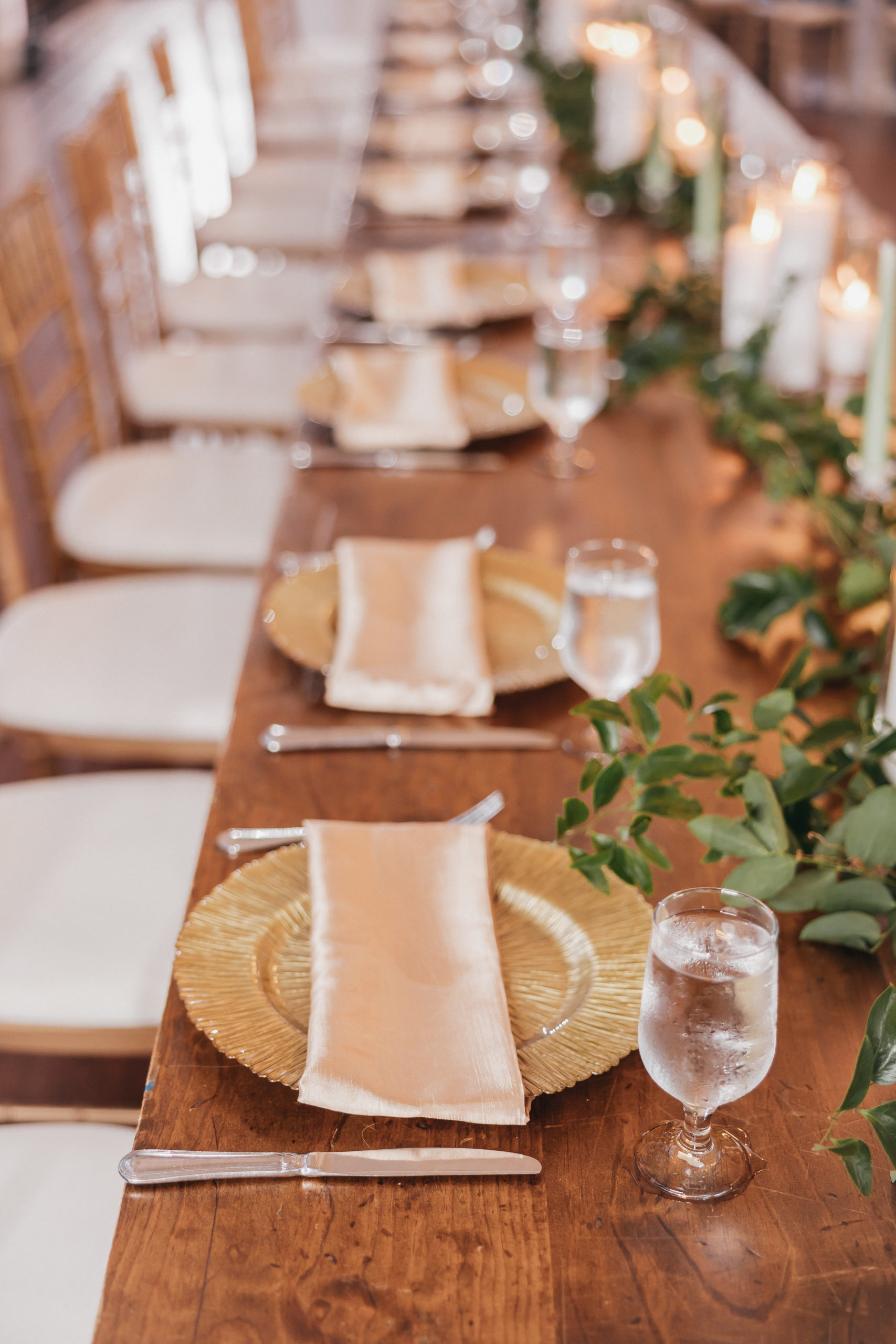 Big Spring Farm Wedding: A Complete Planning Guide. Close-up shot of wooden reception table with gold plates, silverware, glasses and plants.