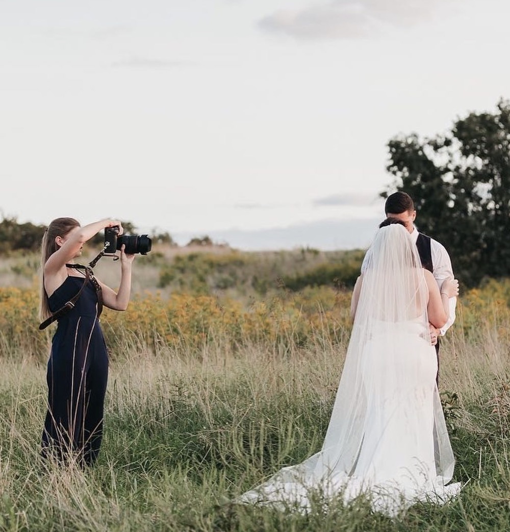 Rachel Yearick taking a photo of bride and groom during their wedding shoot at a field