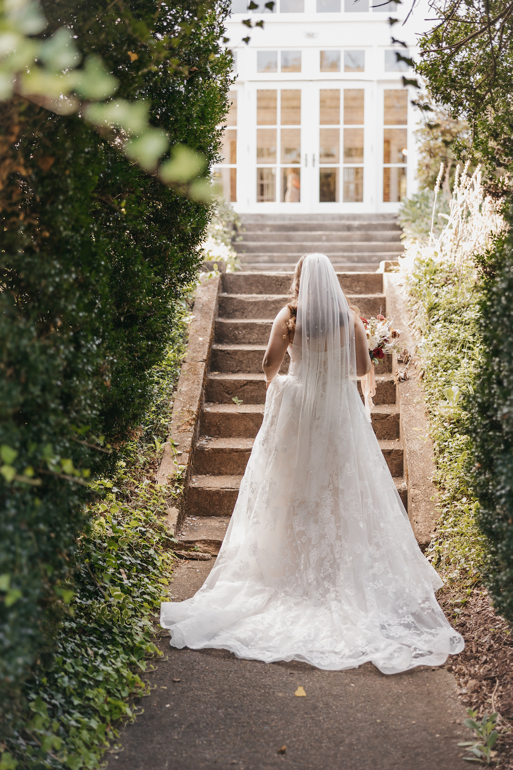 How to Choose a Wedding Photographer (Everything You Need to Know): Bride wearing her dress and veil and approaching a set of stairs with her back to the camera.