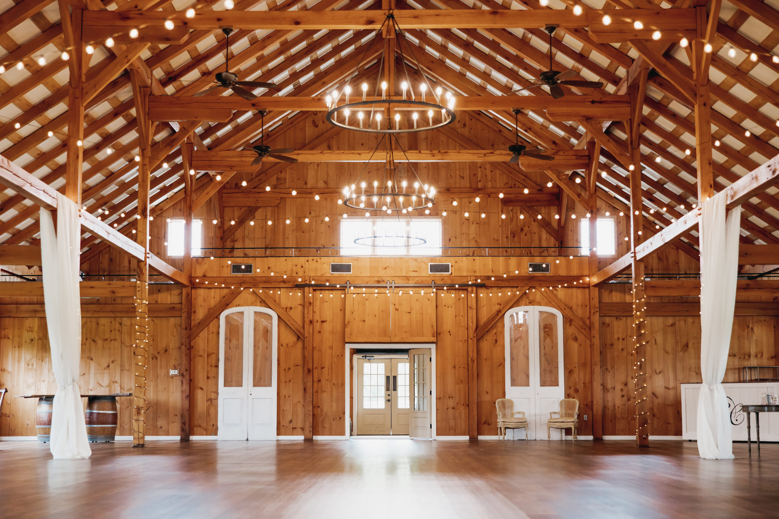 Shadow Creek Wedding Ultimate Planning Guide: Barn ballroom with chandeliers overhead with string lights and curtains draping from wooden beams.