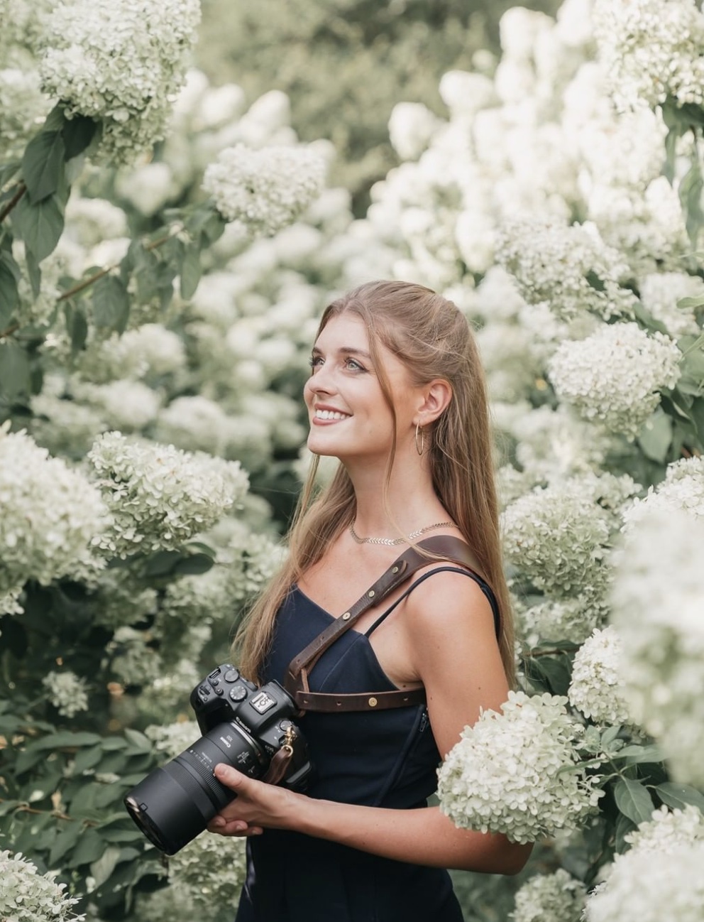 Rachel Yearick posing with her camera in the middle of white flowers at a wedding shoot