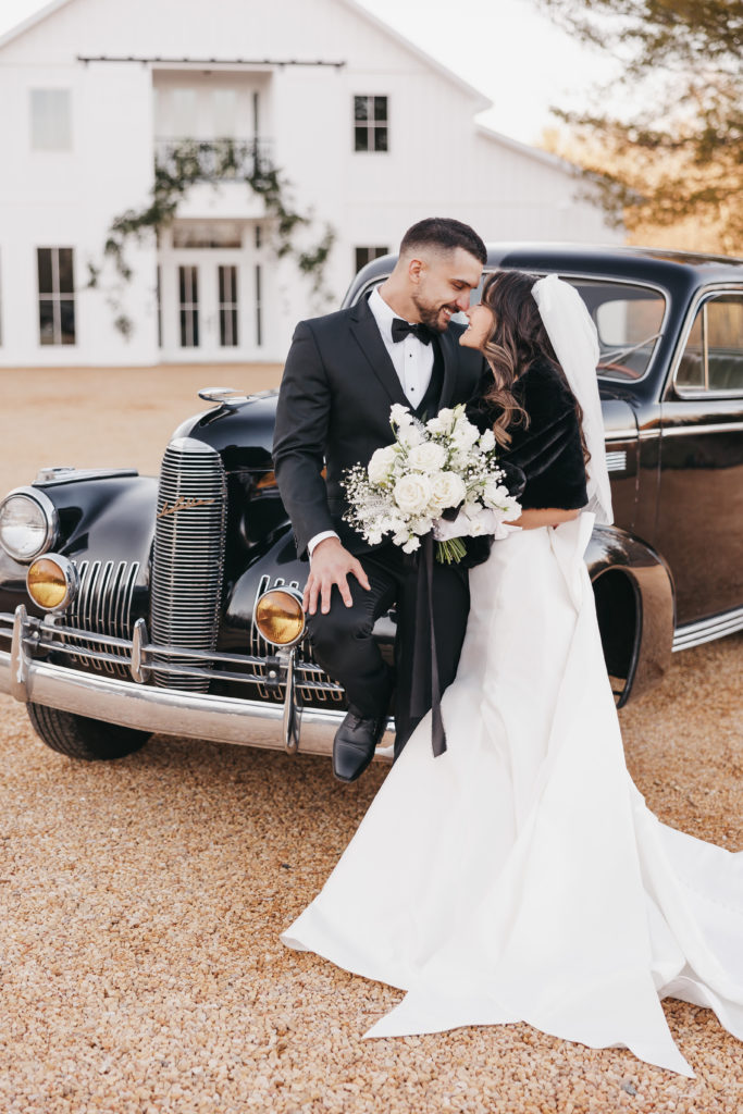 Bride and groom share an embrace and pose next to vintage black car, captured by Rachel Yearick Photography