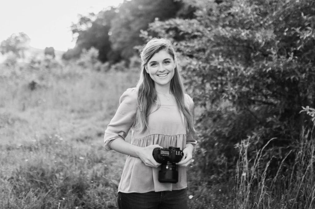 Black and white photo of christian wedding photographer Rachel Yearick smiling while holding her camera