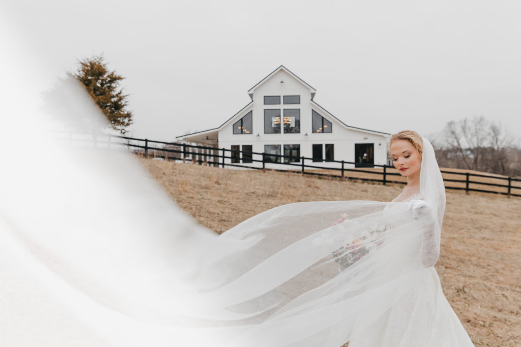 Bride posing in front of venue as her veil sways in the wind, taken by christian wedding photographer Rachel Yearick