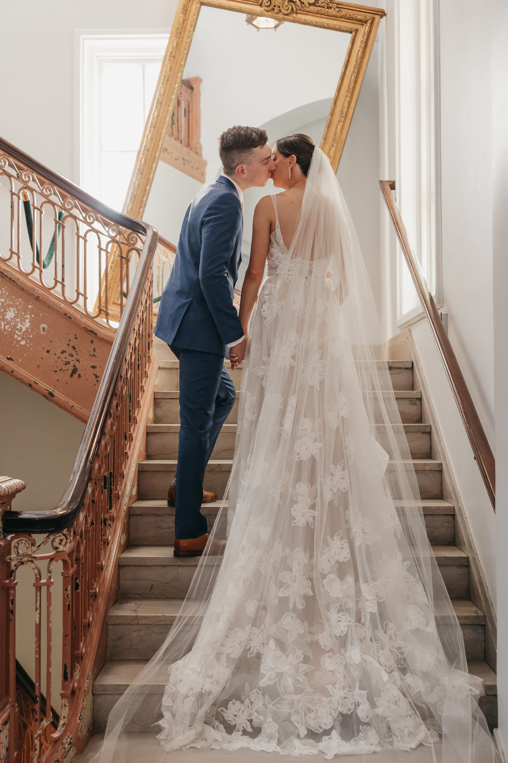 Bride and groom sharing a kiss as they hold hands on the stairs, taken by Rachel Yearick Photography