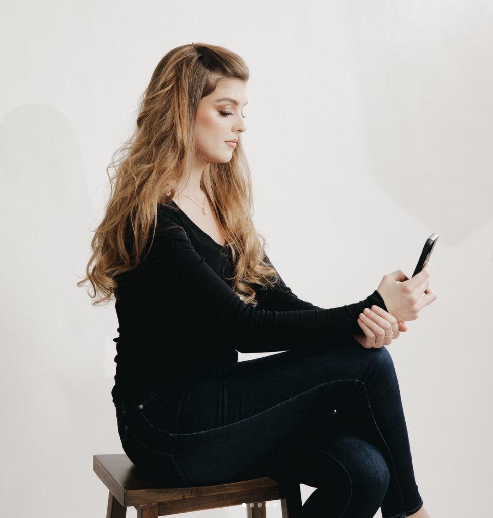 Rachel Yearick sitting on wooden stool and posing with her phone