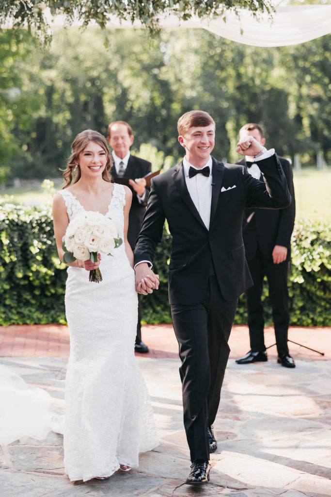 Bride and groom holding hands and smiling as they walk back down the aisle, taken by Rachel Yearick Photography