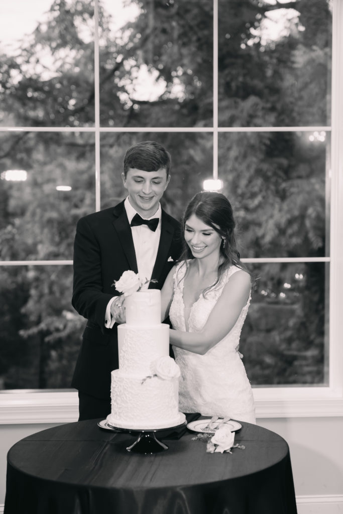 Black and white photo of newlywed couple cutting a slice of their cake during the wedding reception