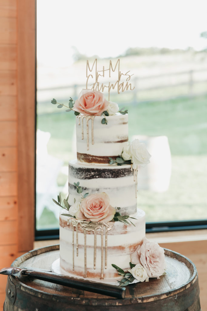 The Barn at Willow Brook Planning And Pricing Guide. Three-tier wedding cake with cake topper set up at the reception.