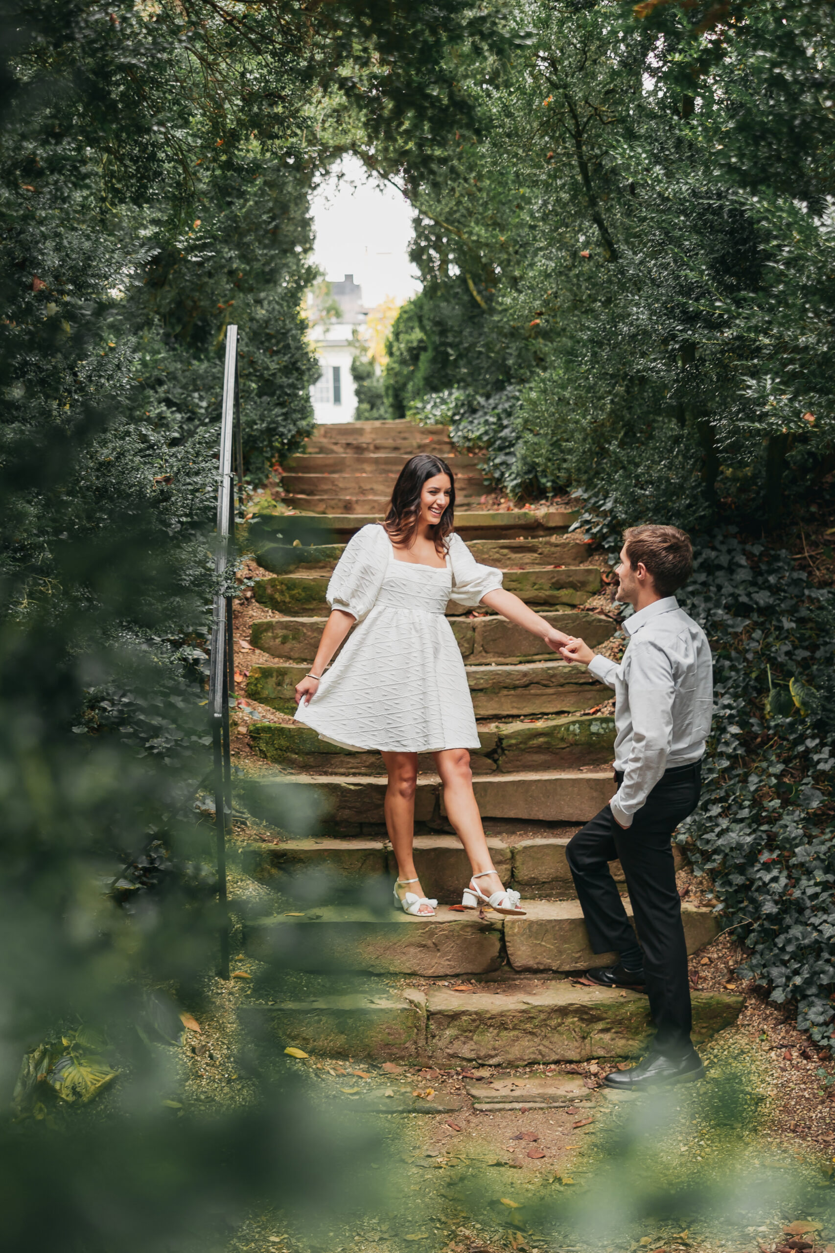 Engaged couple holding hands as they pose in front of stairs, captured by Rachel Yearick Photography