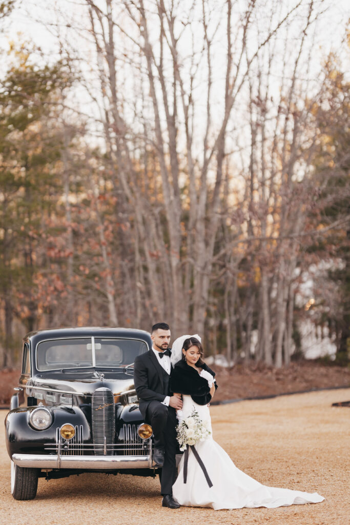 Bride and groom posing next to vintage car, shot by warm wedding photographer Rachel Yearick