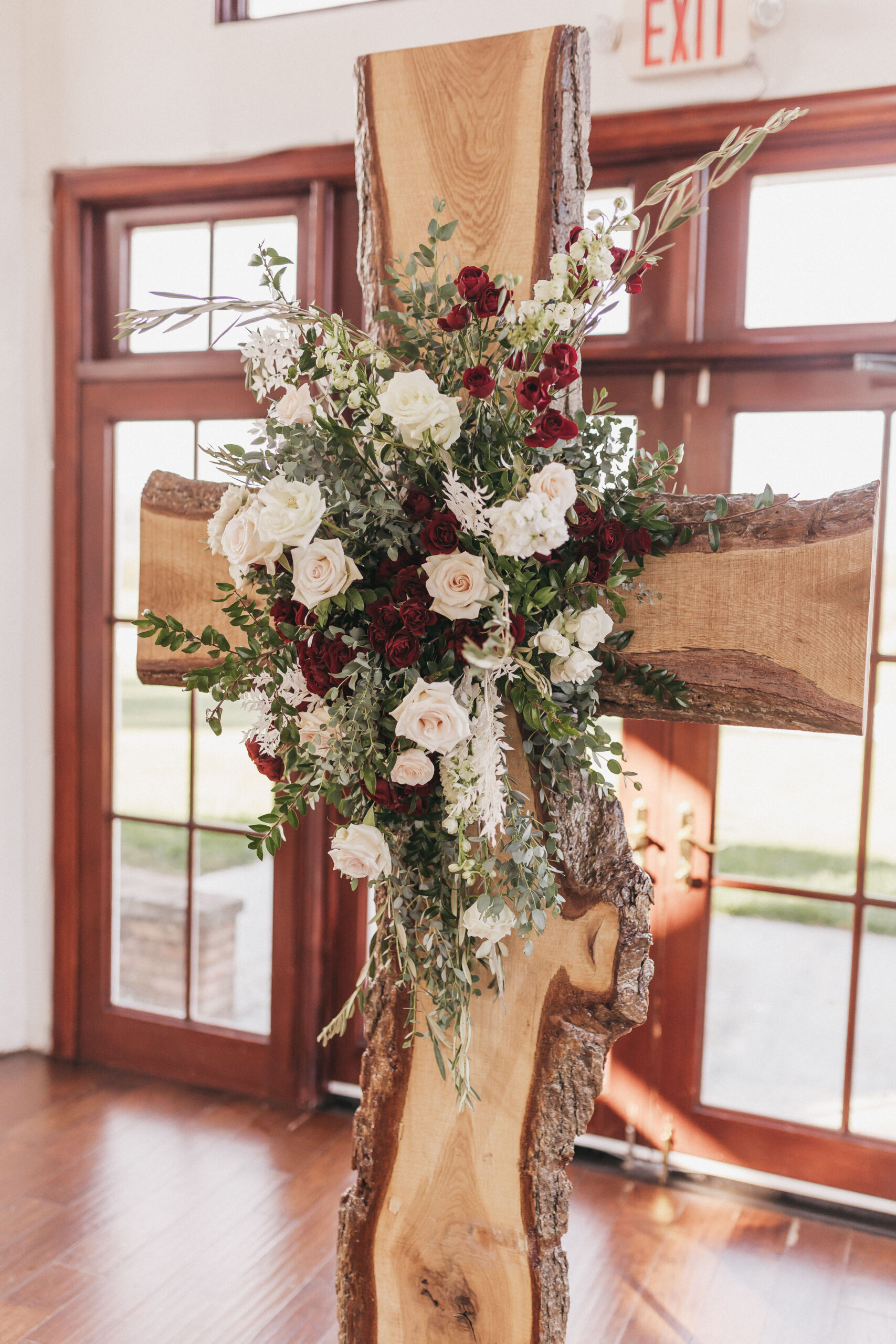 Close-up shot of floral arrangement on wooden cross at the wedding ceremony venue in Raspberry Plain Manor