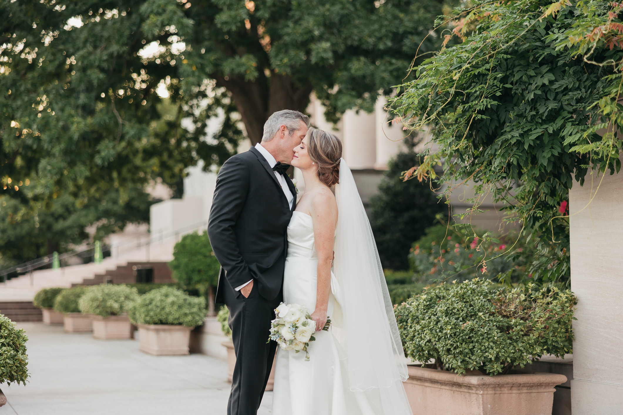 10 Christian Weddings Songs of 2023. Groom planting a kiss on bride's cheek as they stand in the middle of the garden.