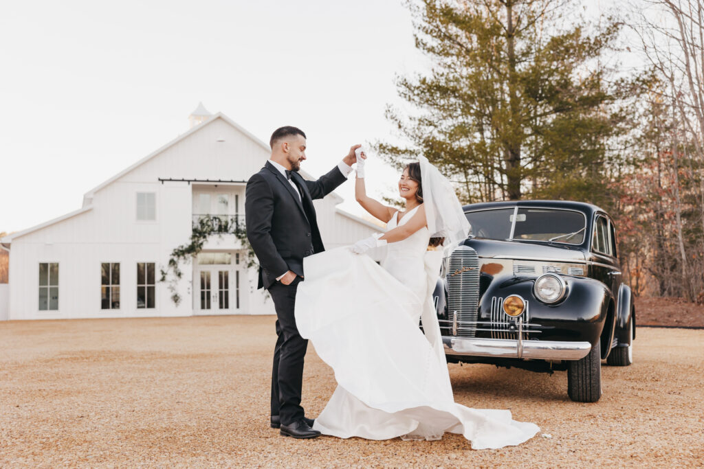 groom twirling his bride in front of a vintage car