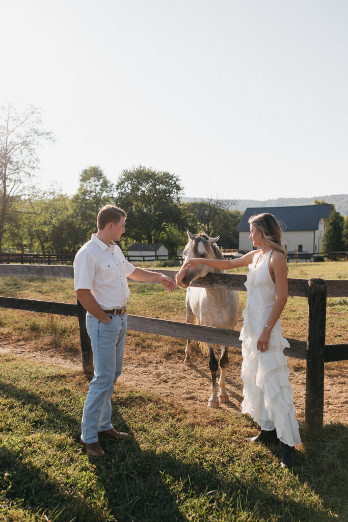 Romantic countryside engagement photo of Olivia and Andrew in Bluemont, Virginia, standing by a wooden fence with a horse under soft golden light.