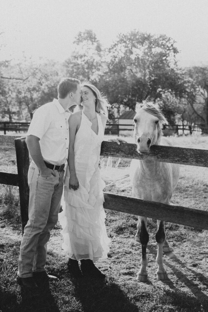 Romantic countryside engagement photo of Olivia and Andrew in Bluemont, Virginia, standing by a wooden fence with a horse.