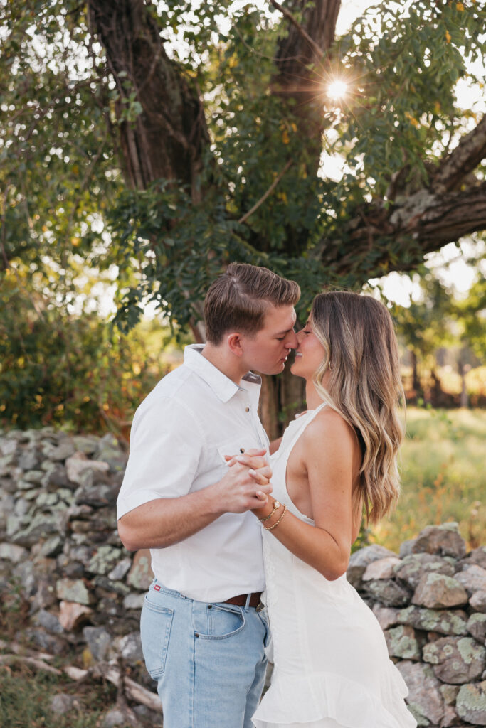 Golden-hour portrait of an engaged couple embracing in an open meadow, surrounded by warm natural light