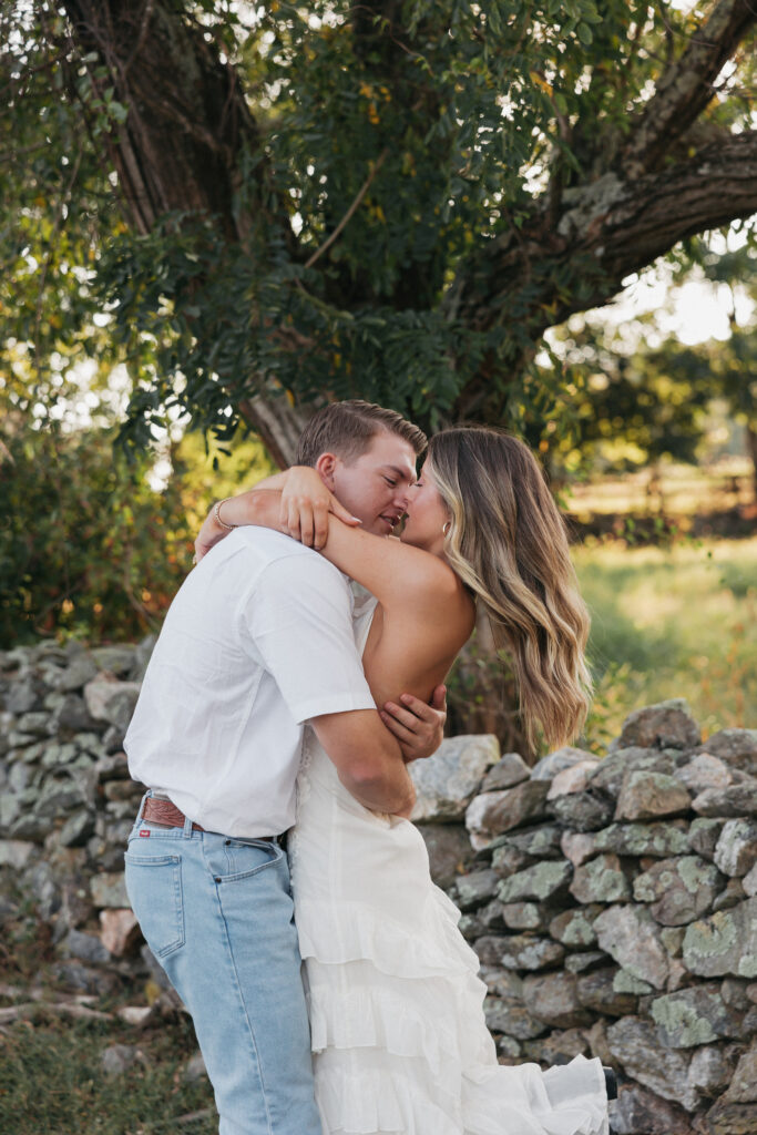 Golden-hour portrait of an engaged couple embracing in an open meadow, surrounded by warm natural light