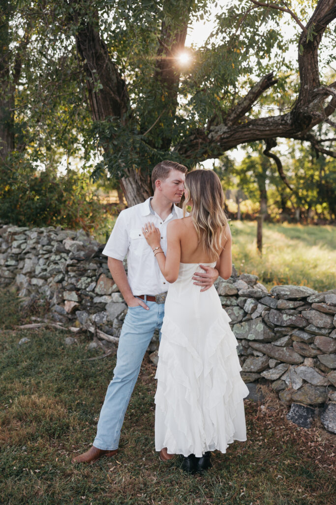 Golden-hour portrait of an engaged couple embracing in an open meadow, surrounded by warm natural light