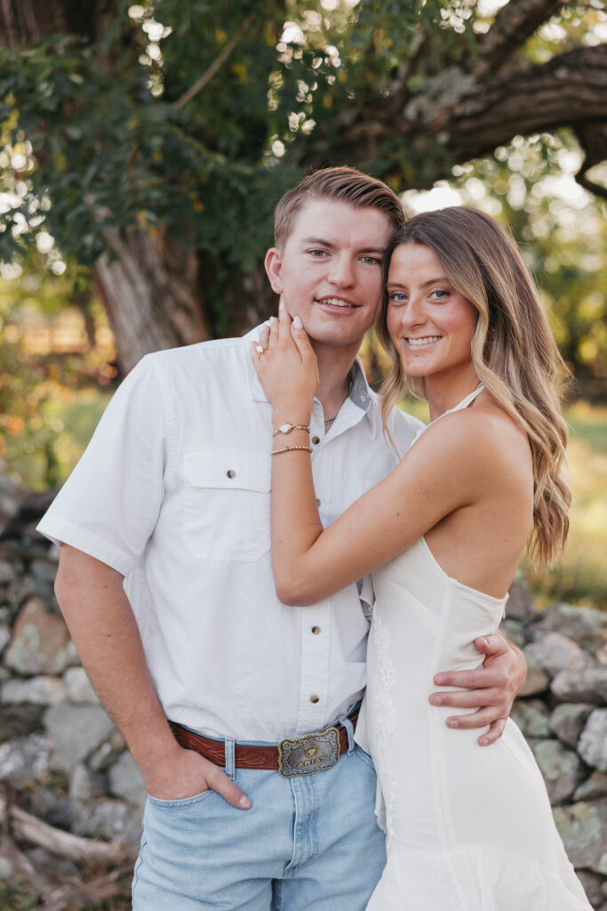 Golden-hour portrait of an engaged couple embracing in an open meadow, surrounded by warm natural light