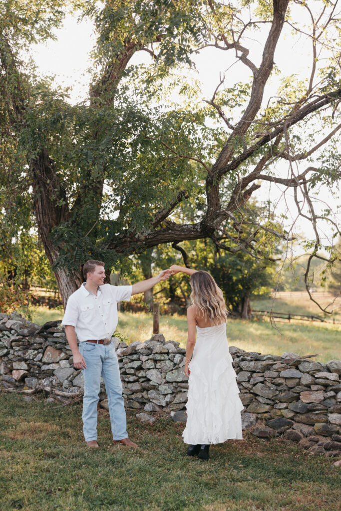 Golden-hour portrait of an engaged couple dancing in an open meadow, surrounded by warm natural light