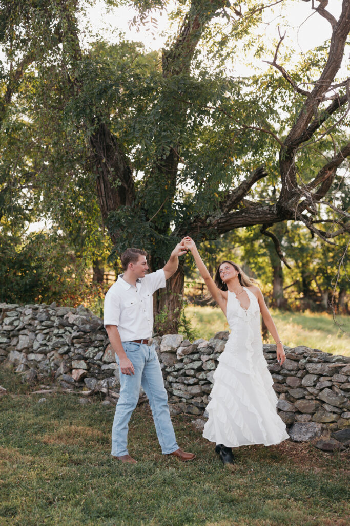 Golden-hour portrait of an engaged couple dancing in an open meadow, surrounded by warm natural light
