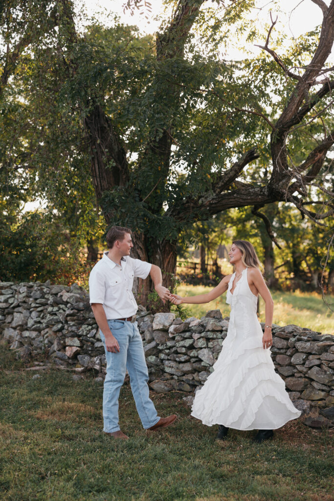 Golden-hour portrait of an engaged couple dancing in an open meadow, surrounded by warm natural light