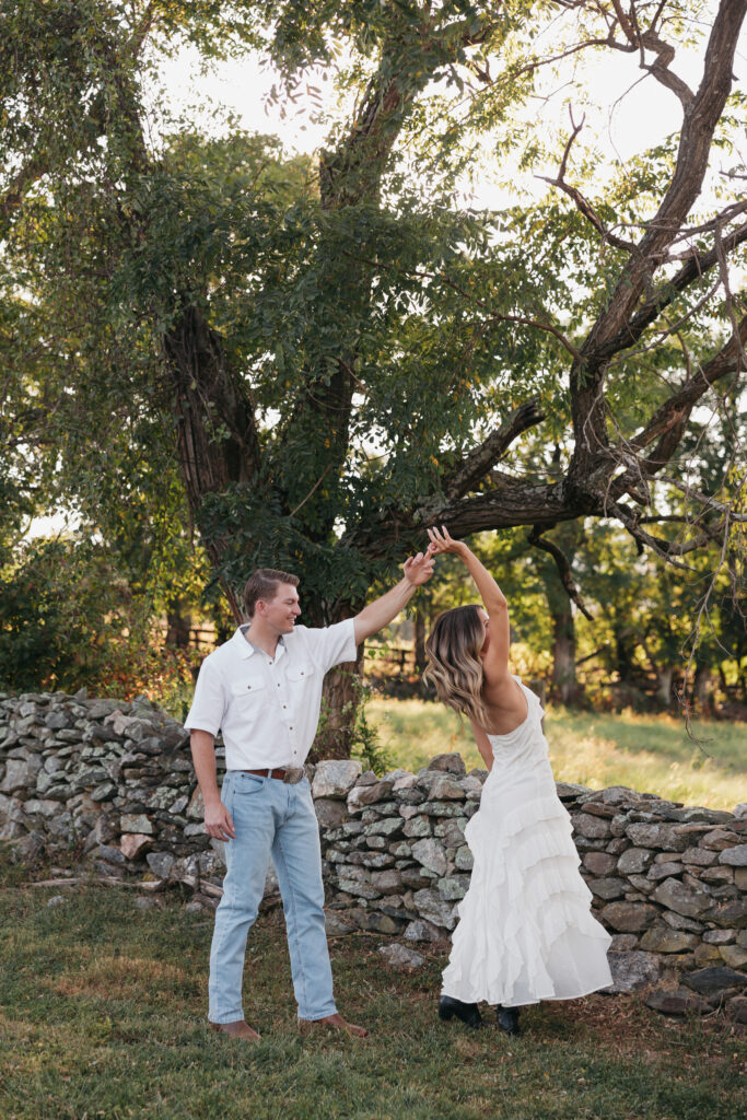 Golden-hour portrait of an engaged couple dancing in an open meadow, surrounded by warm natural light