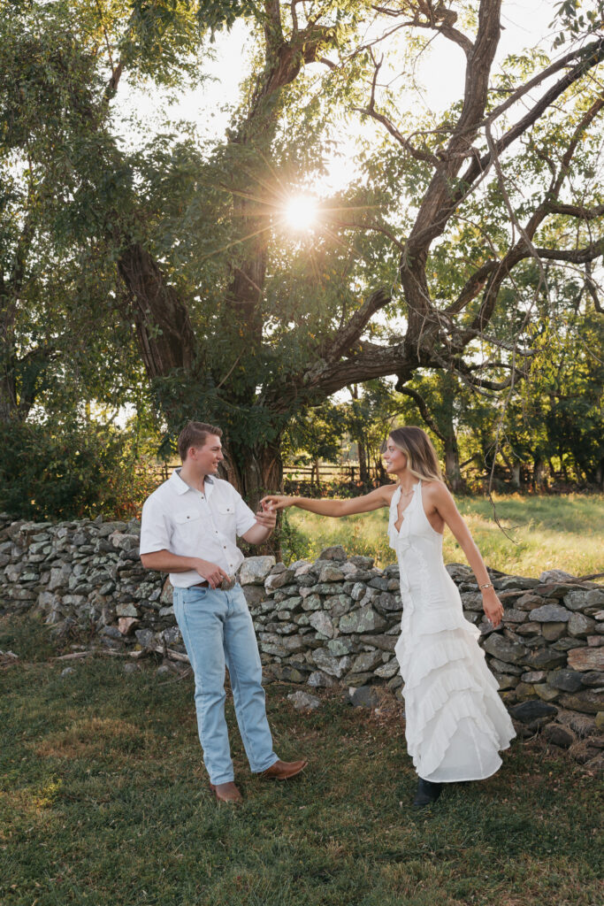 Golden-hour portrait of an engaged couple dancing in an open meadow, surrounded by warm natural light
