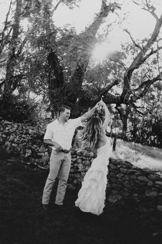 Golden-hour portrait of an engaged couple dancing in an open meadow, surrounded by warm natural light