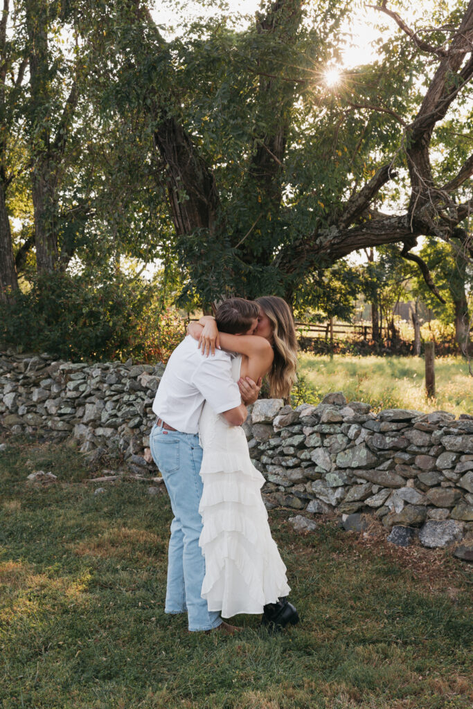 Golden-hour portrait of an engaged couple embracing in an open meadow, surrounded by warm natural light