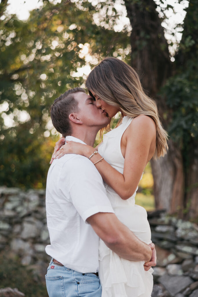 Golden-hour portrait of an engaged couple embracing in an open meadow, surrounded by warm natural light