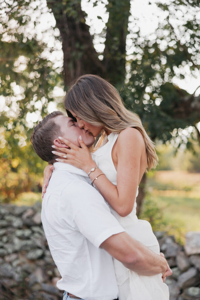 Golden-hour portrait of an engaged couple embracing in an open meadow, surrounded by warm natural light