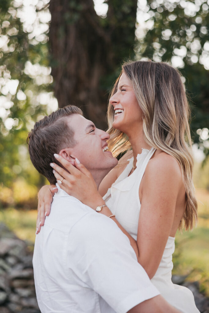 Golden-hour portrait of an engaged couple embracing in an open meadow, surrounded by warm natural light