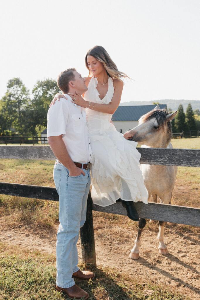 Romantic countryside engagement photo of Olivia and Andrew in Bluemont, Virginia, standing by a wooden fence with a horse under soft golden light.
