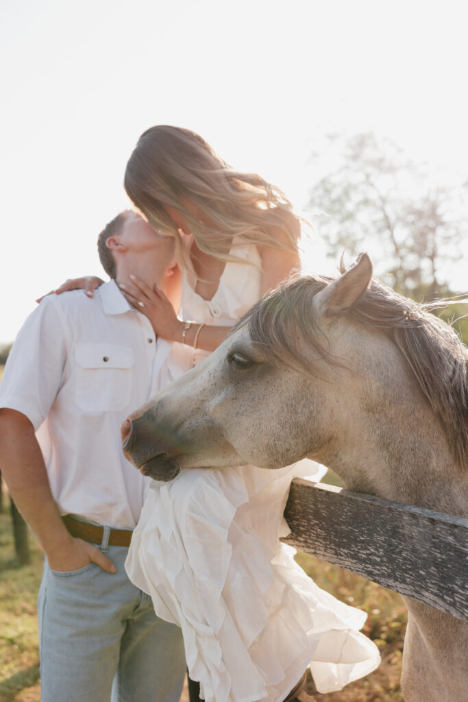 Romantic countryside engagement photo of Olivia and Andrew in Bluemont, Virginia, standing by a wooden fence with a horse under soft golden light.