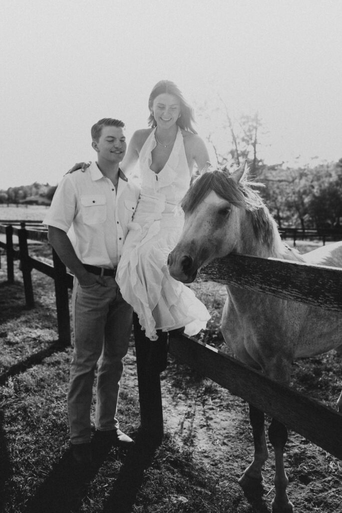 Romantic countryside engagement photo of Olivia and Andrew in Bluemont, Virginia, standing by a wooden fence with a horse under soft golden light.