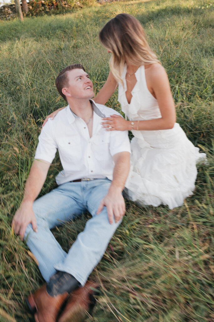 Golden-hour portrait of an engaged couple embracing in an open meadow, surrounded by warm natural light.