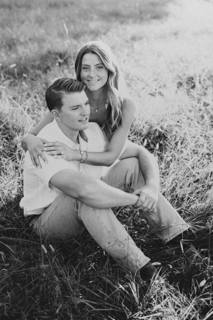 Golden-hour portrait of an engaged couple embracing in an open meadow, surrounded by warm natural light.