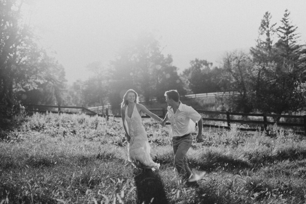 Golden-hour portrait of an engaged couple frolicking in an open meadow, surrounded by warm natural light.