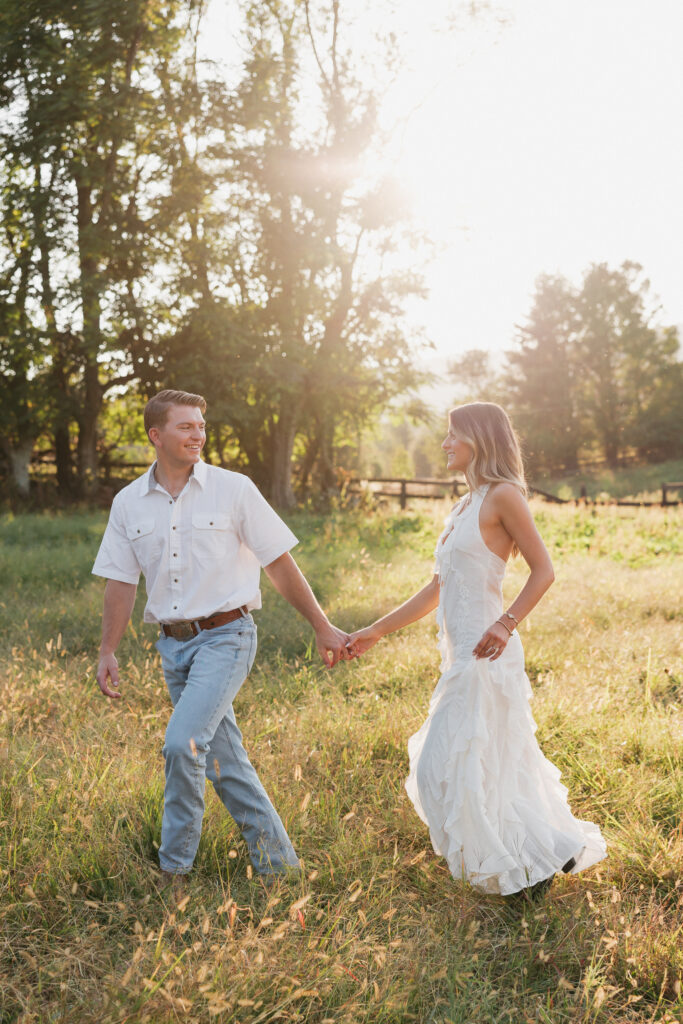 Golden-hour portrait of an engaged couple frolicking in an open meadow, surrounded by warm natural light.