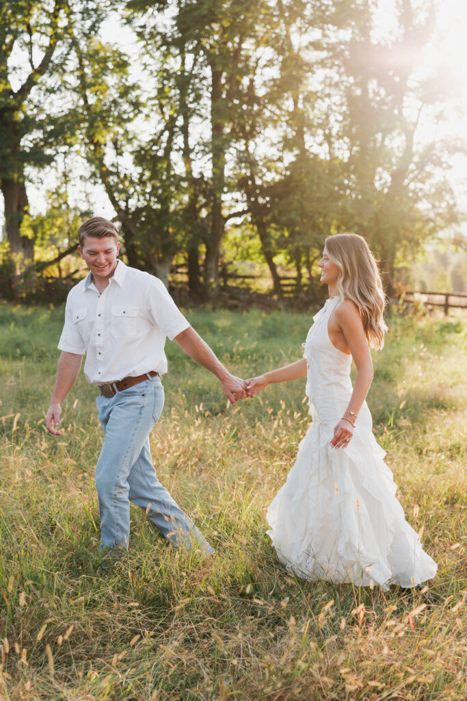 Golden-hour portrait of an engaged couple frolicking in an open meadow, surrounded by warm natural light.