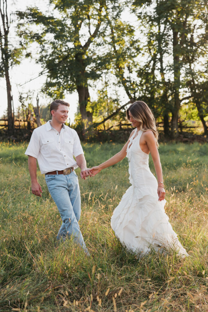 Golden-hour portrait of an engaged couple frolicking in an open meadow, surrounded by warm natural light.